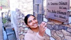 ਆਪਣੀ ਨੇਮ ਪਲੇਟ ਨੂੰ ਦੇਖ ਕੇ ਖੁਸ਼ ਹੁੰਦੀ ਕੁੜੀ ਦੀ ਤਸਵੀਰ 