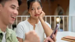 ስልኩ ላይ ያተኮረ ወንድ እና የተከፋ ፊት የምታሳይ ሴት