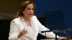 Dina Boluarte, presidenta de Perú, vestida de blanco, habla desde un estrado