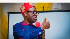 Gomina Chukwuma Charles Soludo ree to fi atanpako ọwọ rẹ juwe bo ṣe n sọrọ pẹlu ẹrọ gbohun-gbohun to mu lọwọ. O de fila pupa, wọ aṣọ alawọ aro