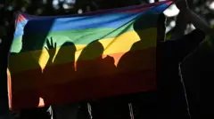 صورة من الخلف لأربعة أشخاص يغطي يقفون أمام علم قوس قزح