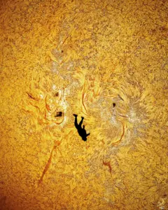 Imagen vertical de la silueta de un hombre en negro y el sol, con sus llamas, de fondo