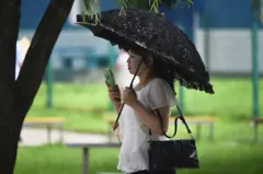 북한 여성이 양산을 쓰고 휴대용 선풍기로 더위를 식히고 있다