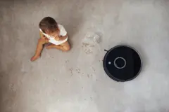 Bebê sentado no chão ao lado de robô aspirador
