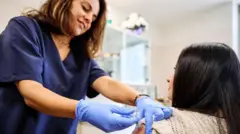 Üzerinde beyaz kazaklı bir kadına grip aşısı yapan mavi eldivenli ve lacivert hemşire elbisesi giren bir kadın hemşire