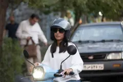 زن ایرانی با لباس سفید سوار بر موتور سیکلت آبی رنگ