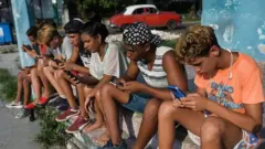 Jóvenes mirando sus celulares en Cuba.