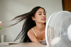 A beautiful Asian woman, feeling overheated, cools herself down with an electric fan 