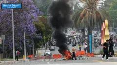 A rua em frente à Home Depot, onde circulavam rumores sobre uma operação contra imigrantes, com carrinhos de compras caídos, algo pegando fogo no meio da via e a placa de Paramount