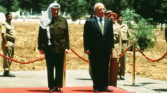 رئيس منظمة التحرير الفلسطينية ياسر عرفات يقف إلى جانب الملك حسين خلال زيارة رسمية في 17 مايو/أيار 1998 في عمّان، الأردن.