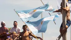 Umufana wa Argentine yuriye ku cyuma cy’itara, mu gihe ikipe y’iki gihugu yatsindiye igikombe cy’isi yanyuraga aho iri muri bisi ifunguye hejuru, i Buenos Aires