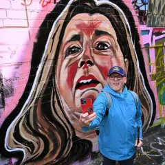 Um homem tirando uma selfie em uma viela de Melbourne em frente a um mural de Erin Patterson