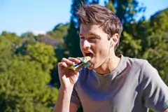 Um homem com fones de ouvindo e comendo uma barrinha de cereal