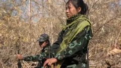 ၂၀၂၄ ခုနှစ်၊ ဖေဖော်ဝါရီလတုန်းက ကရင်နီပြည်နယ်တစ်နေရာမှာ လုံခြုံရေးယူနေတဲ့ KNDF တပ်ဖွဲံဝင်အမျိုးသမီးနှစ်ဦးကို ခြောက်သွေ့နေတဲ့ ကိုင်းတော နောက်ခံနဲ့ မြင်တွေ့ရပါတယ်။