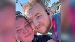 A close up selfie of Richard with his girlfriend, Sophie, at the Race for Life running event. Sophie, on the left, has brown hair and wears sunglasses on the top of her head. Richard is standing next to Sophie with his cheek touching her cheek. He wears a green t-shirt, a pink medal, earphones and has short blonde hair.