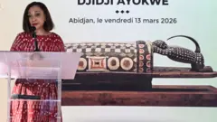 Ivorian Minister of Culture and Francophonie Françoise Remarck talks at a podium in front of a picture of the ornately carved wooden drum