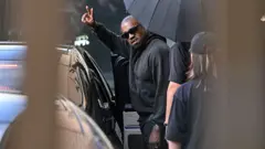 Kanye West for front of car wit Umbrella wey block half im face as e dey wave for China