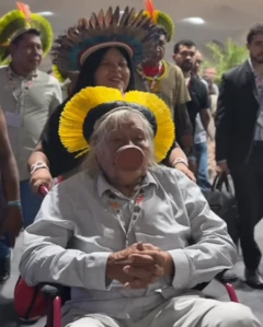 Captura de tela de vídeo postado no Instagram pela ministra Sônia Guajajara, que mostra ela levando Raoni, sentando em uma cadeira de rodas, para uma reunião com autoridades. Ambos usam cocares coloridos e Raoni veste uma camisa de manga longa de cor gelo