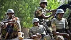 Awọn ọmọ ologun to wa ninu asọ khaki wọn de ate sori, wọ ẹwu ayẹta, wọn si gbe ibọn lọwọ, gbogbo wọn joko sori ọkọ ijagun