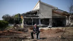 Un hombre está sentado frente a una casa en el centro de Israel que resultó dañada por un proyecto lanzado por Hezbolá desde el Líbano (12 de marzo de 2026)