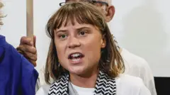 Greta Thunberg veste uma camiseta branca e um lenço estampado enquanto fala