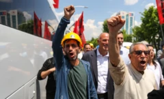 Sarı kasklı bir madenci ve yanındakiler sağ kolllarını havaya kaldırmış ve yumruk yapmış. Slogan atarak yürüyorlar.