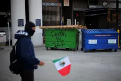 Persona con la bandera de México y un cartel que dice "Muerte al ICE" en un cajón de la basura.