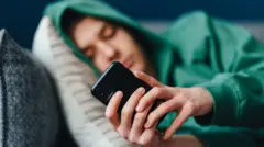 Jovem usando celular deitado no sofá