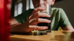 Підліток сидить за столом, тримає перед собою склянку з колою 