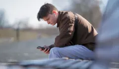 Un joven usa su teléfono móvil mientras está sentado en un banco de un parque en un día despejado en Vladimir.