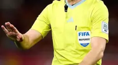sarı formalı bir FIFA hakeminin gövdesinden bir kesit, elini ileri uzatmış