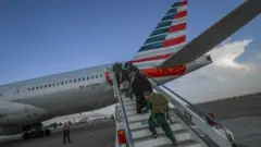 Pessoas embarcando em avião com bandeira americana estampada na parte traseira
