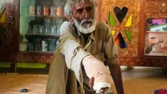 Siahouk, with his hand bandaged, sitting on the floor of his home