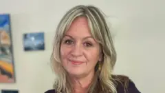 Uma mulher de cabelos longos e loiros olha para a câmera.