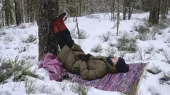 Mari Ahonen deitada sobre um pano colorido sobre a neve em meio a árvores.