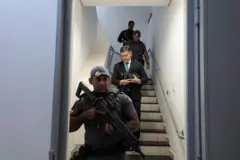 Lincoln Gakiya descendo escadas e sendo escoltados por policiais armados 