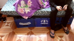 Pessoa mexendo em celular e sentada em cima de 'cama' feita com engradados de cerveja