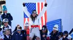 Бризи Джонсон с золотой медалью держит флаг США в окружении команды.