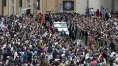 Papa Francisco em carro cercado por uma multidão de fiéis
