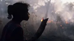 অস্ট্রেলিয়ার আর্নহাম ল্যান্ডের একটি মেয়ে একটি ছোট ডালে আগুন ধরিয়েছে।