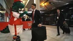 Mesut Ozil greeted by mascot Gunnersaurus before a Champions League tie against Paris St-Germain in 2016