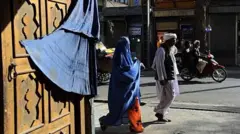 تصویر یک زن که با چادری که در کنار مردی در شهر هرات قدم می‌زند. 