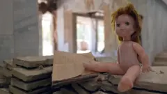 A doll sits on the remains of books in abandoned city