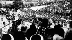 Uma fotografia em preto e branco de Abdul Hamid 2º, de 1908, andando numa carruagem puxada por cavalos e rodeado por uma multidão