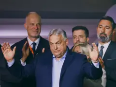 Viktor Orban con los brazos abiertos. Tras él hay un grupo de cuatro personas. 