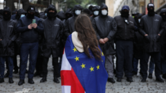 زن جوانی با پرچم گرجستان و اتحادیه اروپا در مقابل صف پلیس ضد شورش ایستاده است