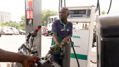 Foto of fuel attendant as e dey pump petrol into one motorcycle for fuel station for Abuja
