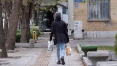 زنی در حالی که کیسه های خریدش را در دست دارد، در پیاده رو راه می رود