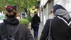 امرأتان تمشيان في الشارع وتواجهان الكاميرا - إحداهما ترتدي الحجاب والأخرى ليست كذلك