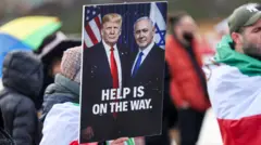 Una persona sujeta un cartel con la foto de Trump y Netanyahu y un texto que dice (en inglés): "La ayuda está en camino".